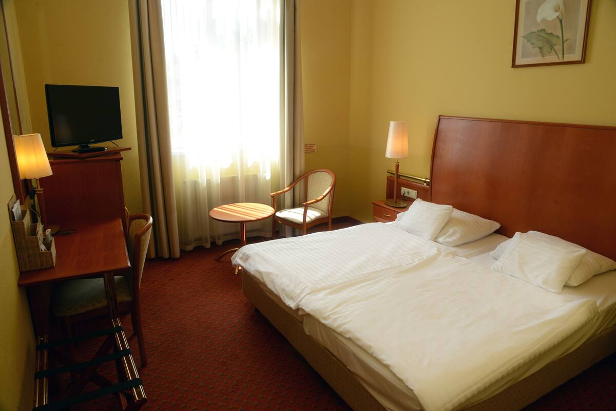 Una habitación de hotel con cama, escritorio, silla, televisor y ventana con cortinas.