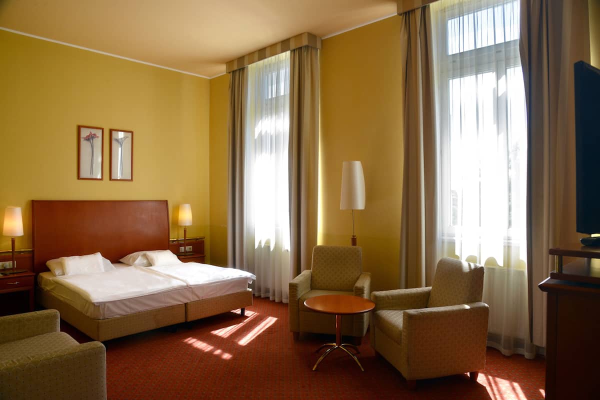 Una habitación de hotel con una cama grande, dos sillones, una mesita y una lámpara.