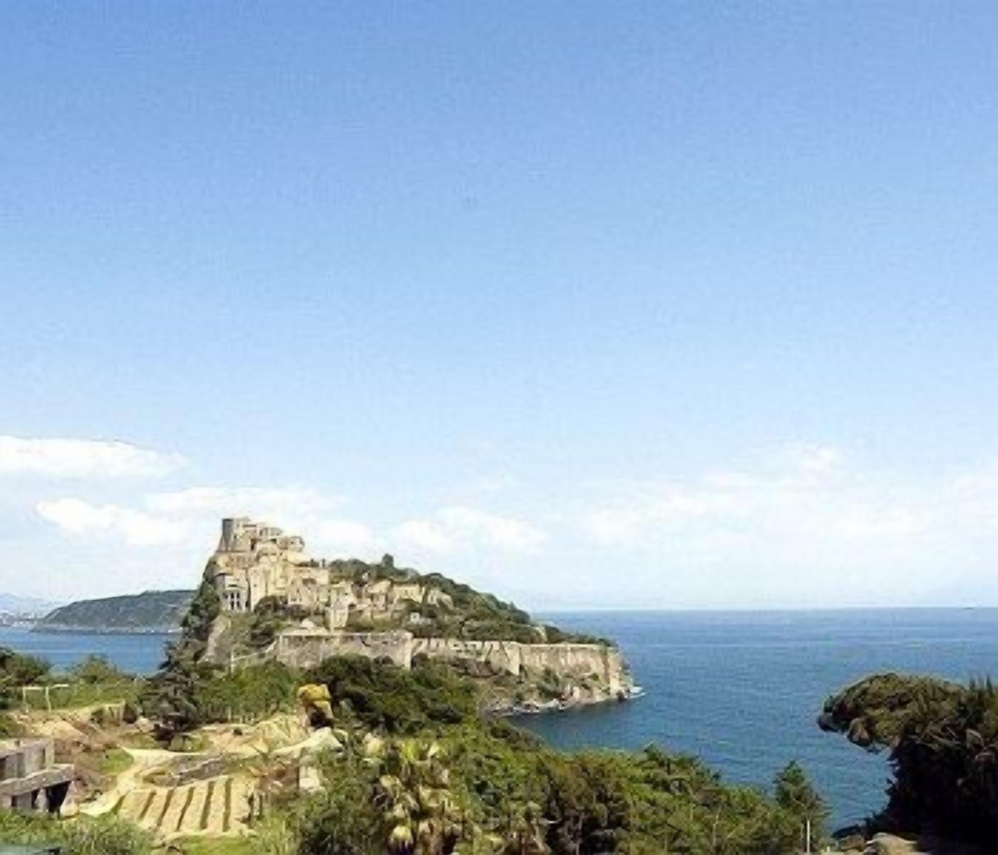 A coastal castle with a fortified structure, surrounded by greenery and overlooking the sea.