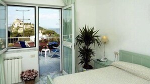 Un dormitorio con cama, una planta en maceta, una mesita de noche y vistas al balcón exterior.