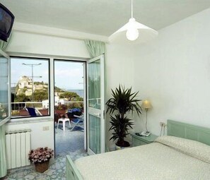 A bedroom with a bed, a potted plant, a nightstand, and a view of the outside balcony. - Parco Cartaromana (Ischia)