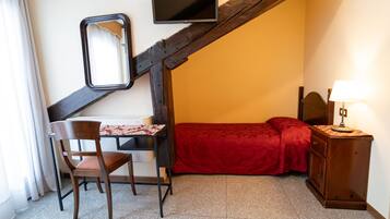 Ein Schlafzimmer mit Bett, Schreibtisch mit Stuhl, an der Wand montiertem Fernseher und Nachttisch mit Lampe.