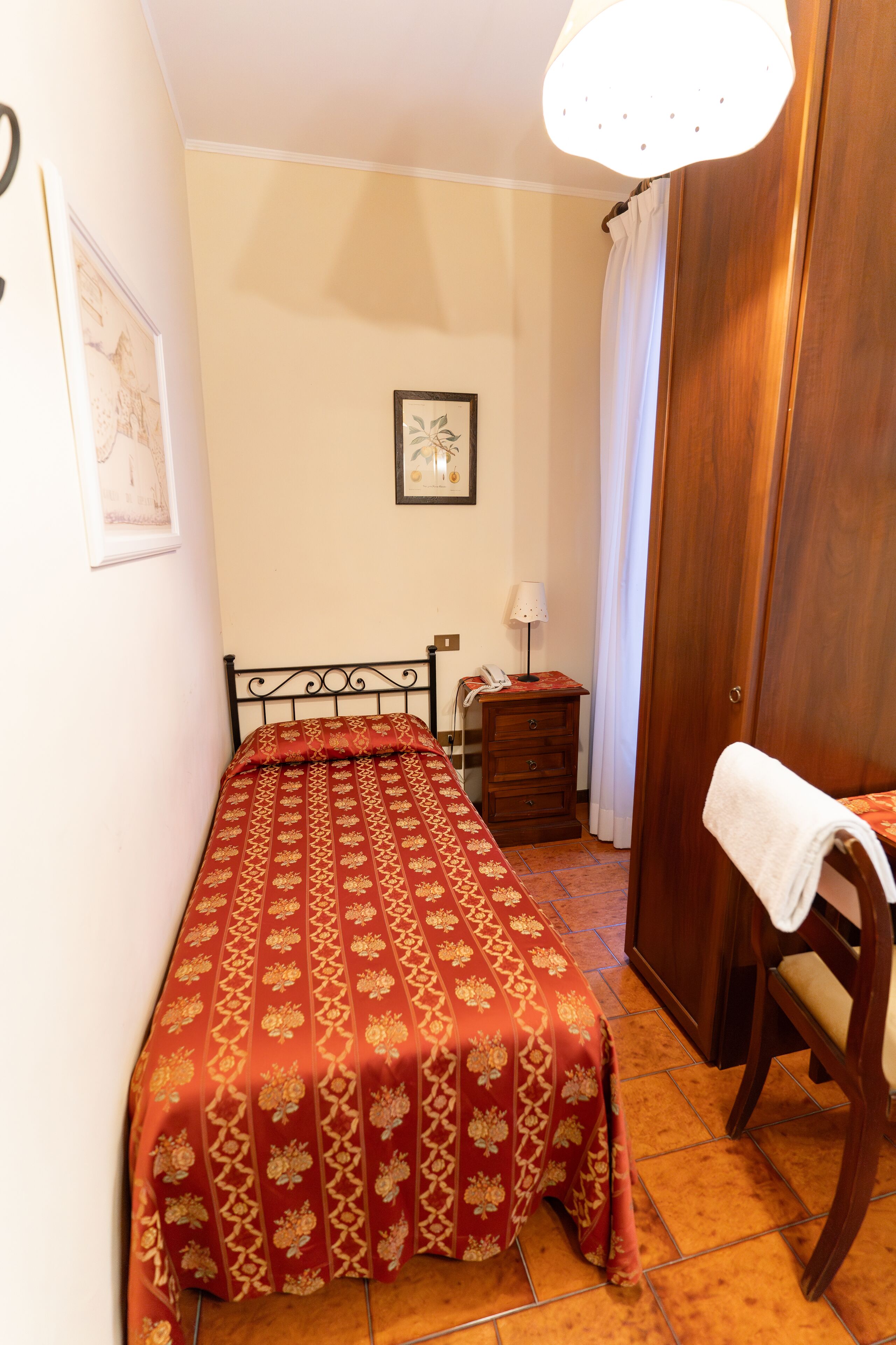Une petite chambre à coucher, bien rangée, avec un lit simple, une table de chevet en bois, une chaise et une armoire.