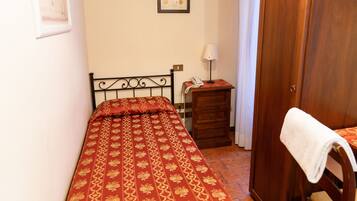 A small, neatly arranged bedroom with a single bed, a wooden nightstand, a chair, and a wardrobe.