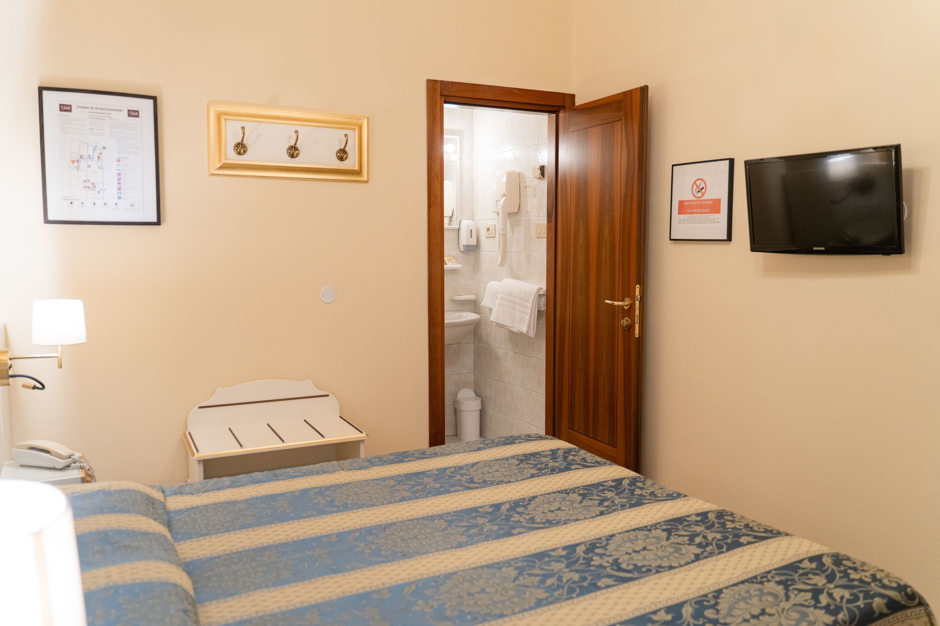 Habitación de hotel con cama, puerta de madera, mesita de noche blanca, televisor de pared y un certificado enmarcado en la pared.