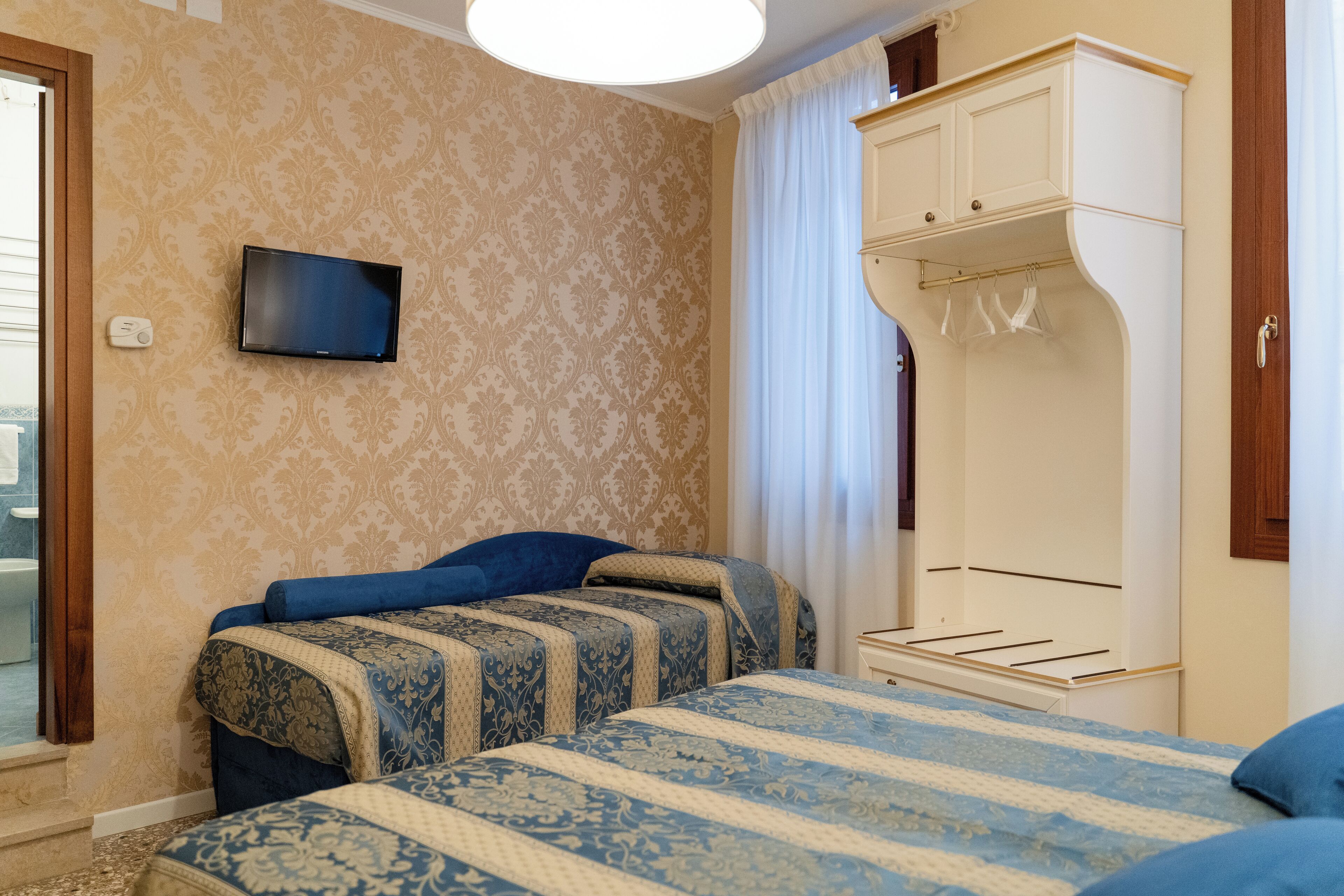 Habitación de hotel con dos camas, televisión, armario y ventana con cortinas.