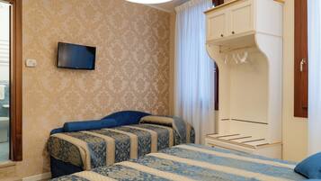 Habitación de hotel con dos camas, televisión, armario y ventana con cortinas.