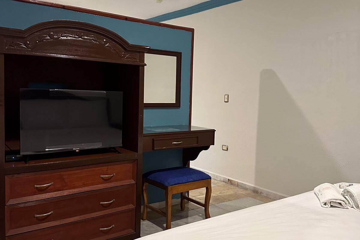 A bedroom with a bed, a wooden dresser with a television, a desk, and a chair.