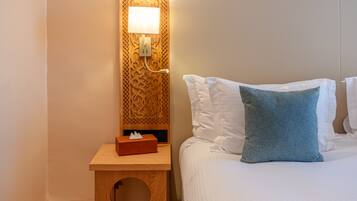 A neatly made bed with white and blue pillows, a bedside table with a tissue box, and a wall-mounted lamp.