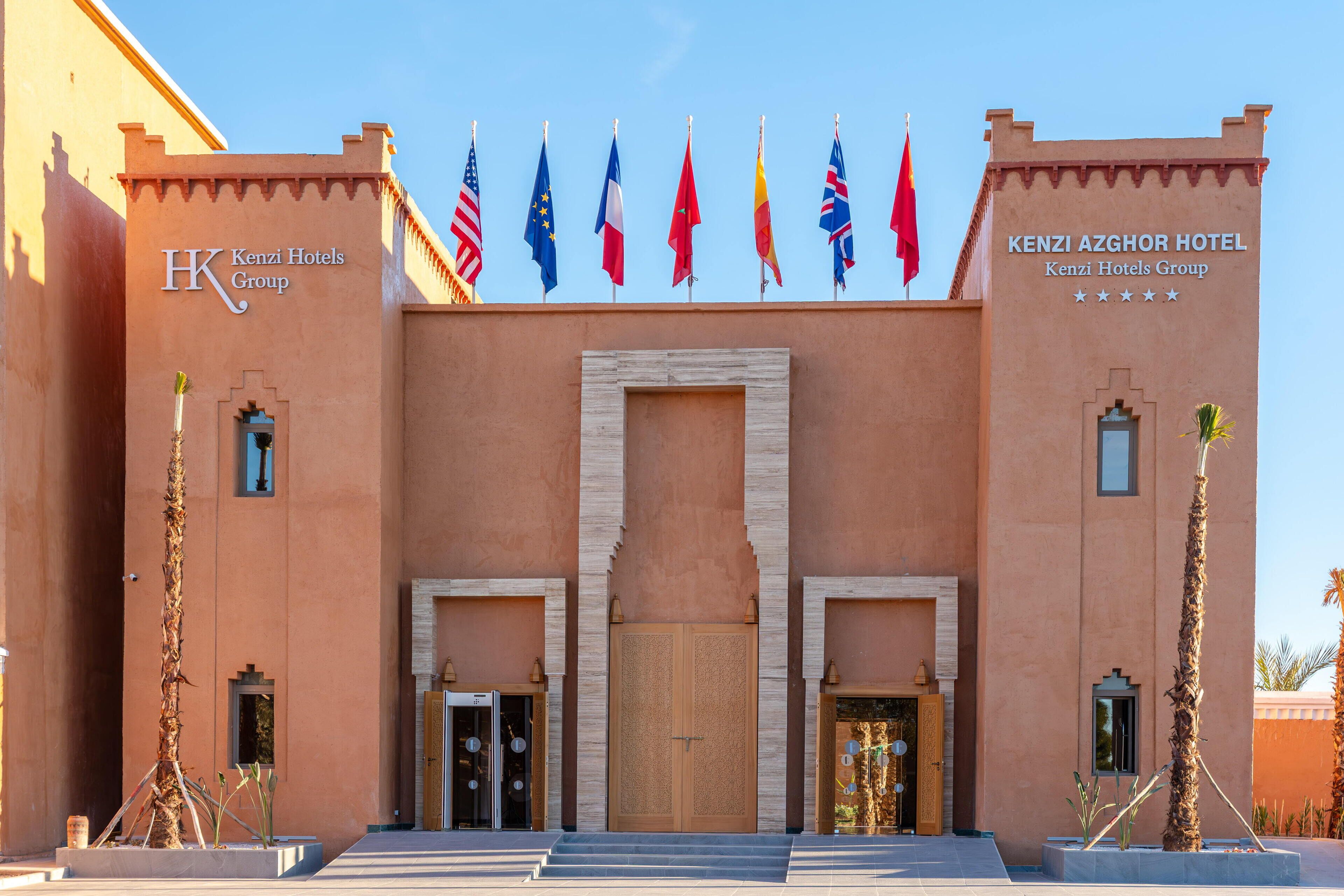 The Kenzi Azghor Hotel entrance with multiple flags, a prominent entrance, and a symmetrical facade.