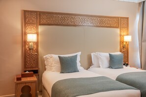 A hotel room with two beds, each with white linens and blue pillows. There are wall-mounted lamps on either side of the beds. - Kenzi Azghor (Ouarzazate)