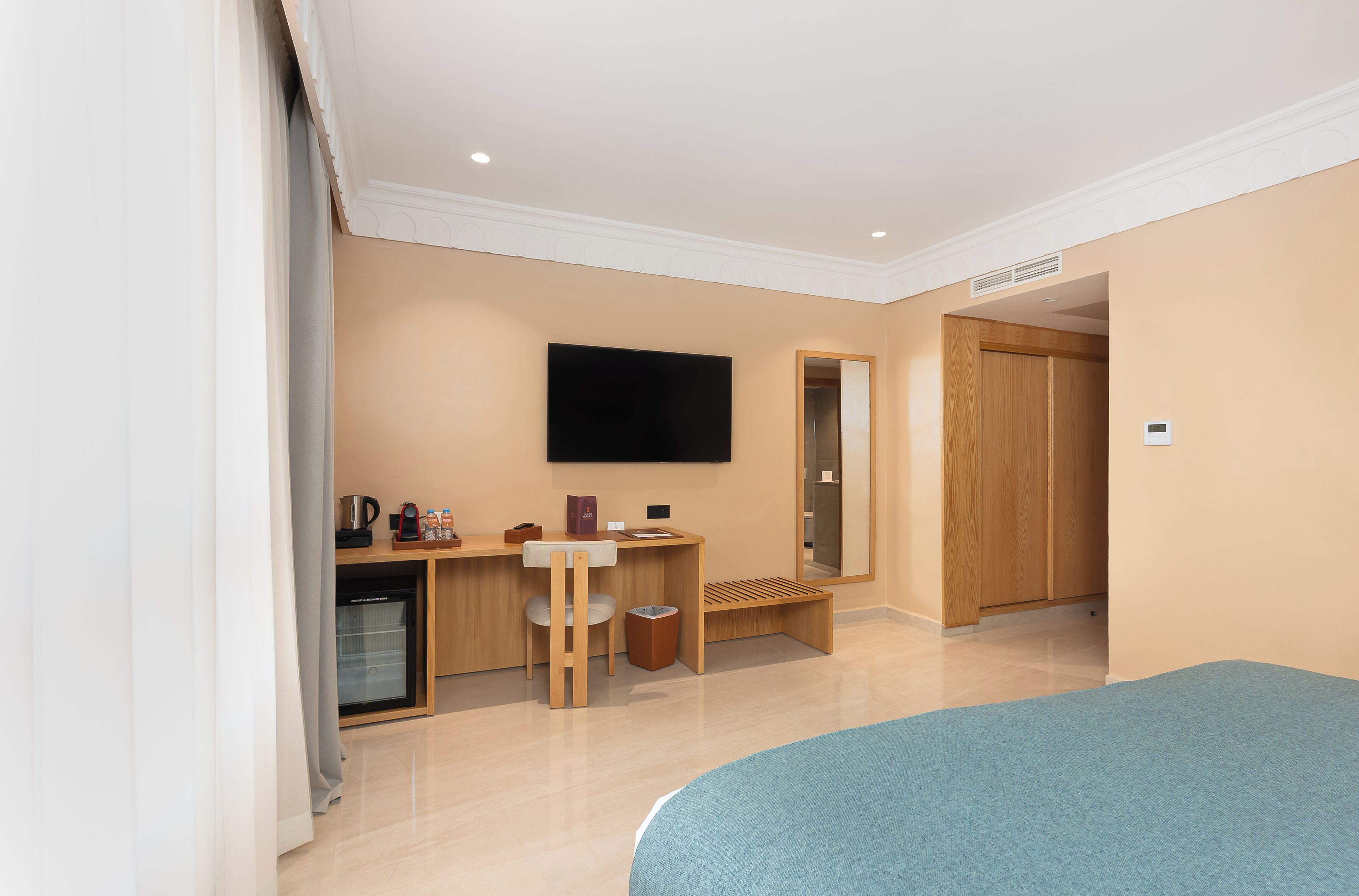 Habitación de hotel con cama, escritorio con silla, televisor, armario y una pequeña kitchenette.