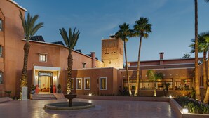 A courtyard with palm trees, a fountain, and a building with a tower. - Kenzi Azghor (Ouarzazate)