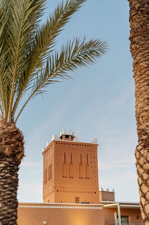 A building with intricate architectural details, including a tower with decorative elements and a flat-roofed structure. - Kenzi Azghor (Ouarzazate)