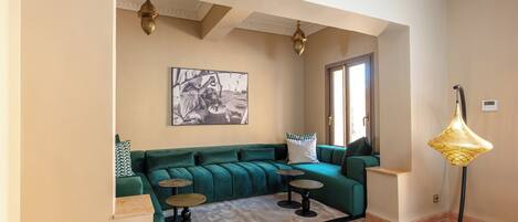 Un salon avec un canapé de couleur turquoise, deux petites tables rondes, un lampadaire et un tableau encadré accroché au mur.