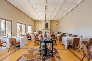 A spacious dining area with multiple tables and chairs, a central serving cart, and large windows allowing natural light.