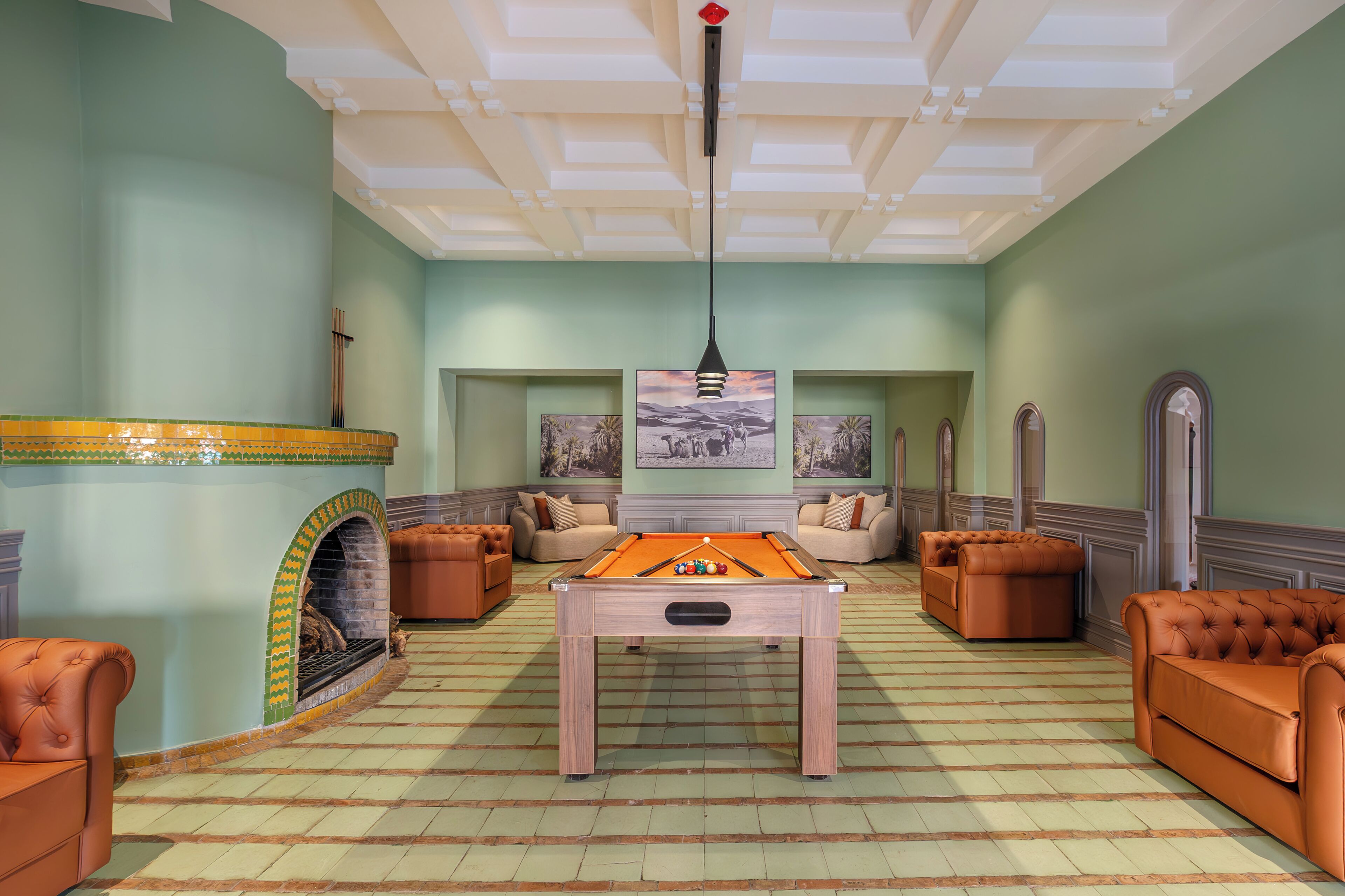 A pool table in a room with green walls, a fireplace, and leather sofas.