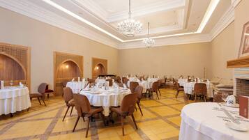 A spacious banquet hall with multiple round tables set for dining, featuring white tablecloths and brown chairs.
