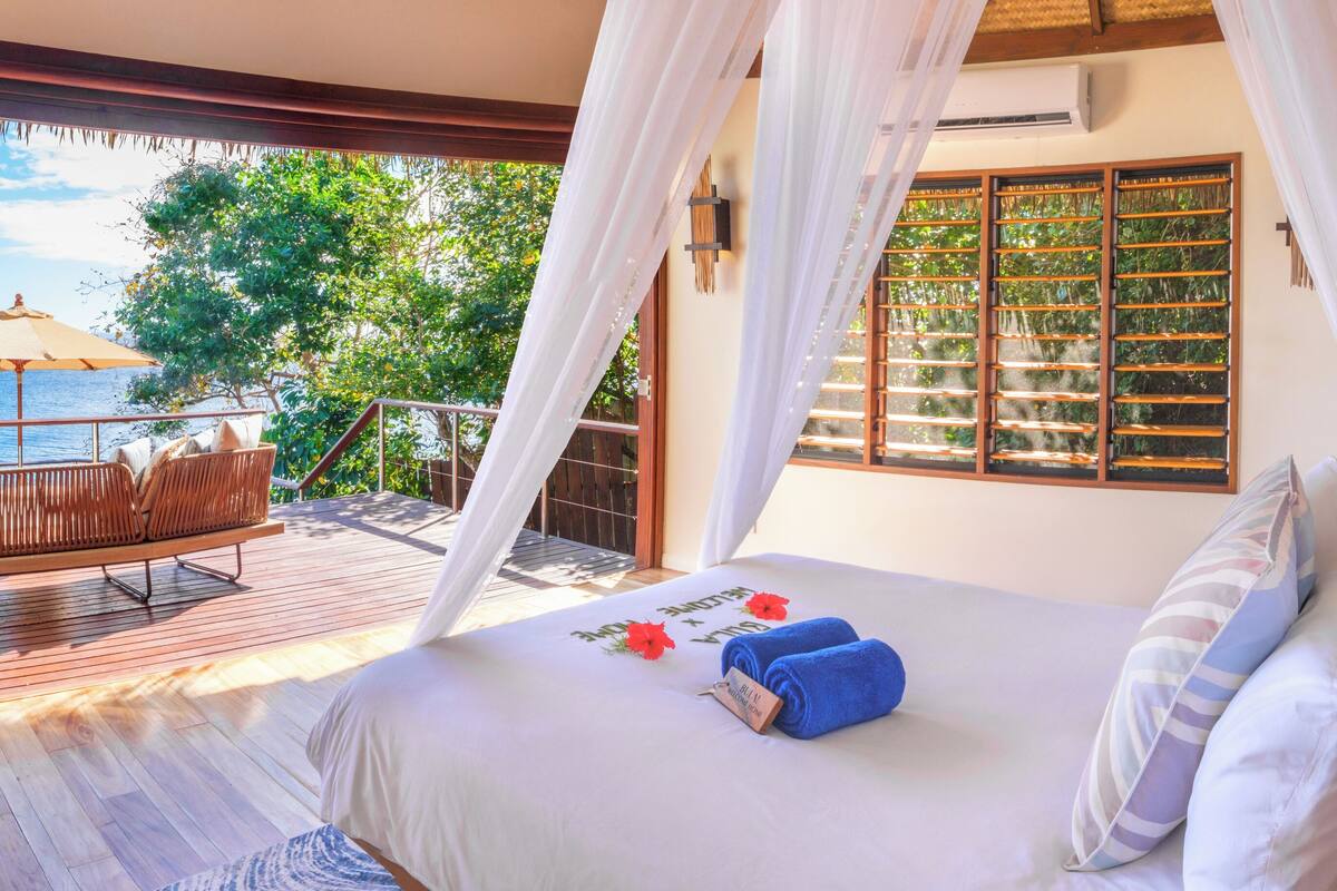 Ein Schlafzimmer mit einem Bett, einer Sitzbank und Blick auf den Ozean.