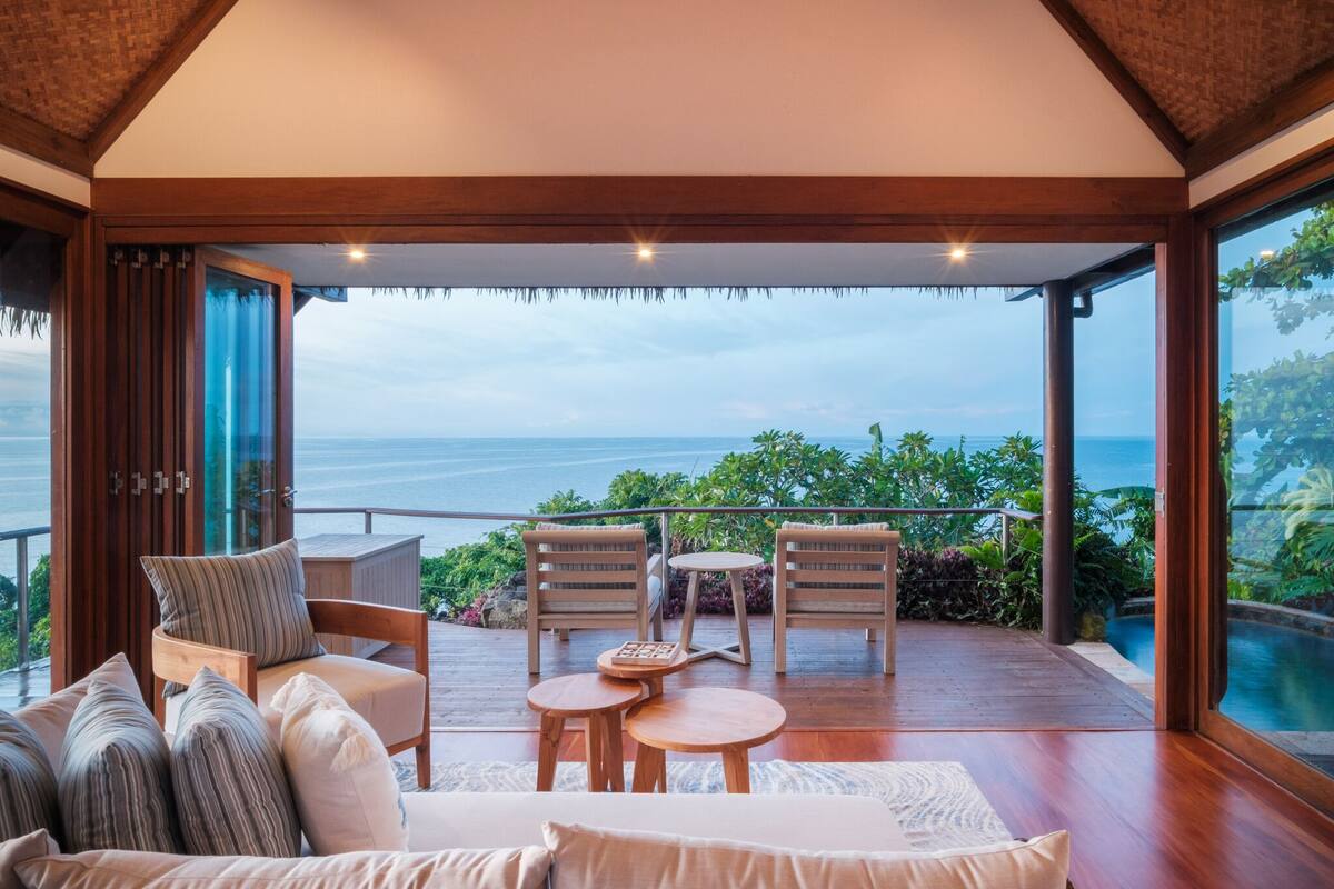 Ein geräumiger Balkon mit Holzmöbeln, Blick aufs Meer und üppigem Grün.
