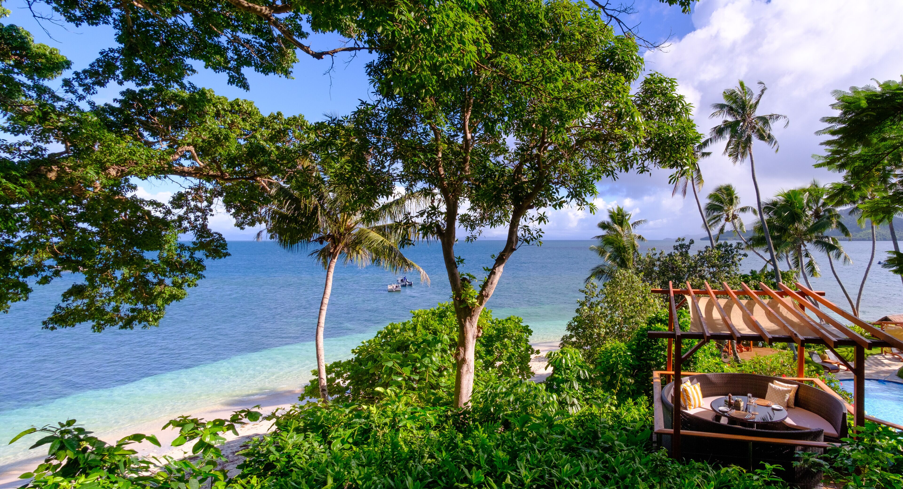 A tropical beach view with a wooden deck and a lounge area overlooking the ocean.