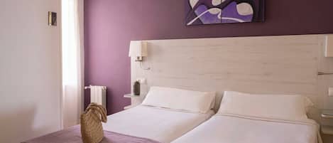 A double bed with white linens, a woven basket, and a purple throw.