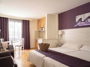 A hotel room with a bed, a desk, a chair, a microwave, and a painting on the wall. - Ona Princesa Playa (Marbella)
