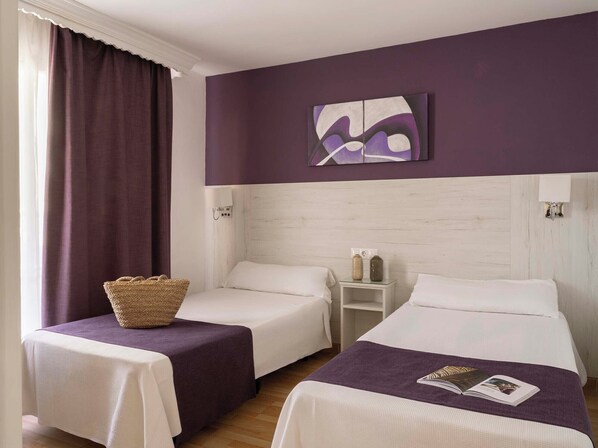 Habitación de hotel con dos camas, una mesita de noche, un cuadro colgado en la pared y una ventana con cortinas.