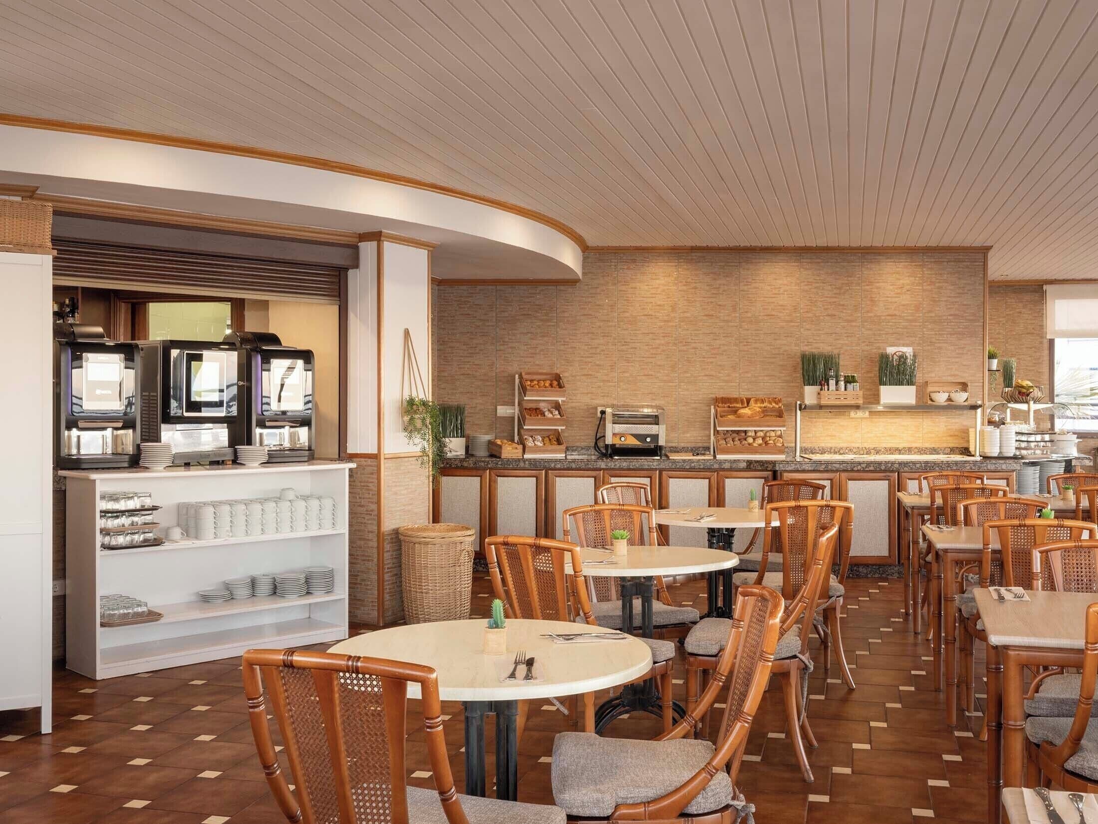 Un restaurante con mesas redondas y sillas de mimbre, una barra de café con máquinas de espresso y un fondo de pared de ladrillo.