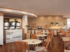 Een restaurant met ronde tafels en rieten stoelen, een koffiebar met espresso machines, en een achtergrond van een bakstenen muur.