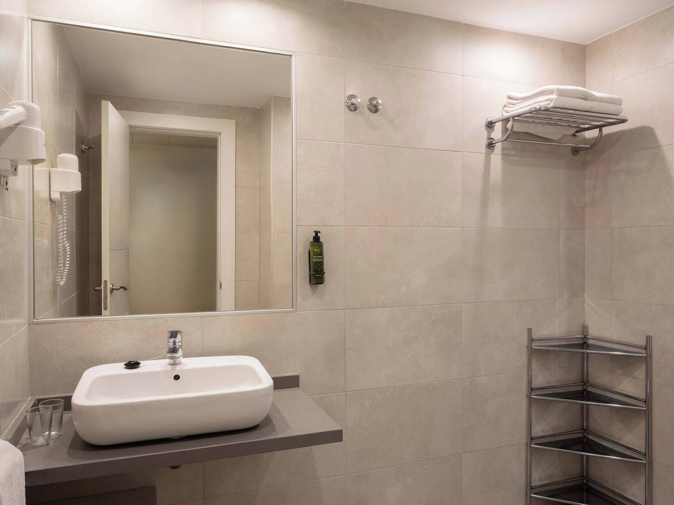 Un baño moderno con un lavamanos blanco, un espejo, zona de ducha y un perchero para toallas.