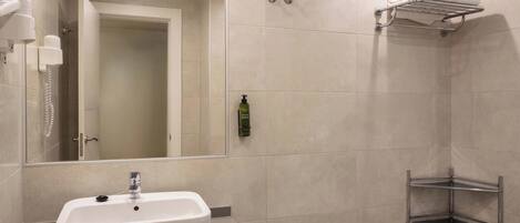 Un baño moderno con un lavamanos blanco, un espejo, zona de ducha y un perchero para toallas.