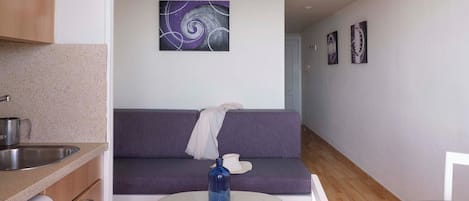 A compact living space with a kitchenette, a sofa, a small round table, and a wall-mounted artwork.