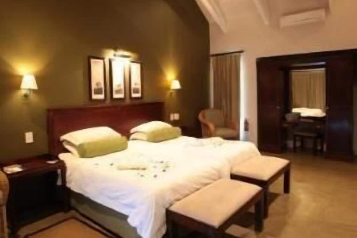 A hotel room with two beds, a bench, a nightstand, and a chair.