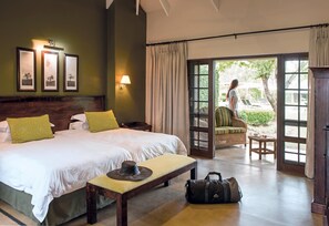 A hotel room with a large bed, a bench, a suitcase, and a view of the outdoors through a glass door.
