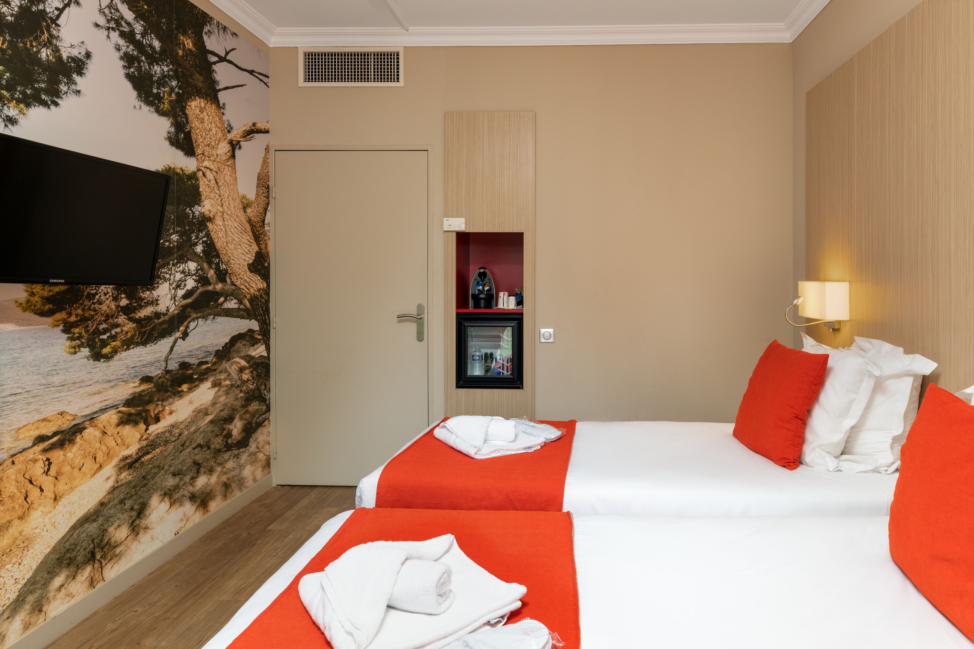Habitación de hotel con dos camas, un televisor, un estante en la pared y una puerta.