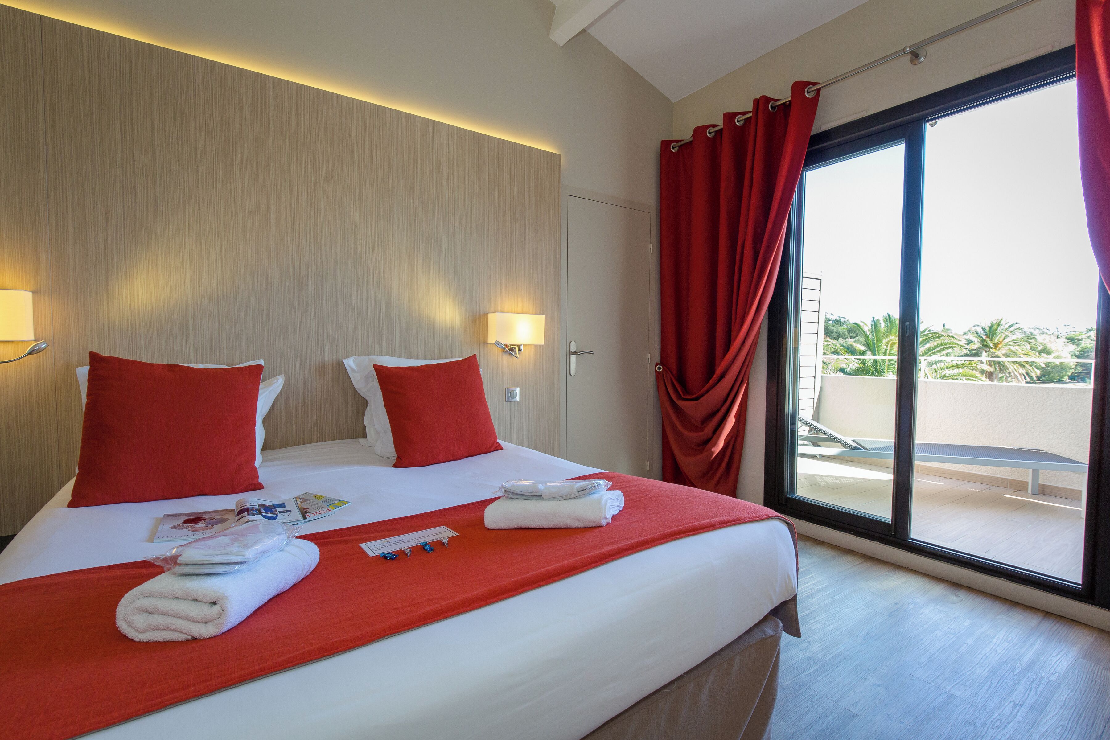 A hotel room with a large bed, red curtains, and a view of the outdoors.