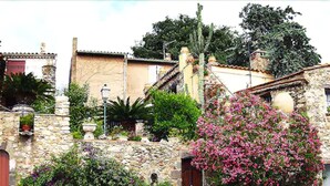 A stone building with a wooden door, surrounded by lush greenery and flowering plants. - SOWELL HOTELS Golfe de Saint-Tropez (Grimaud)