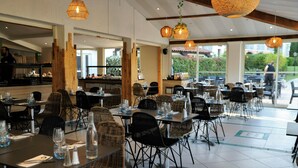 A restaurant with multiple tables and chairs, large windows, and hanging wicker lamps. - SOWELL HOTELS Golfe de Saint-Tropez (Grimaud)