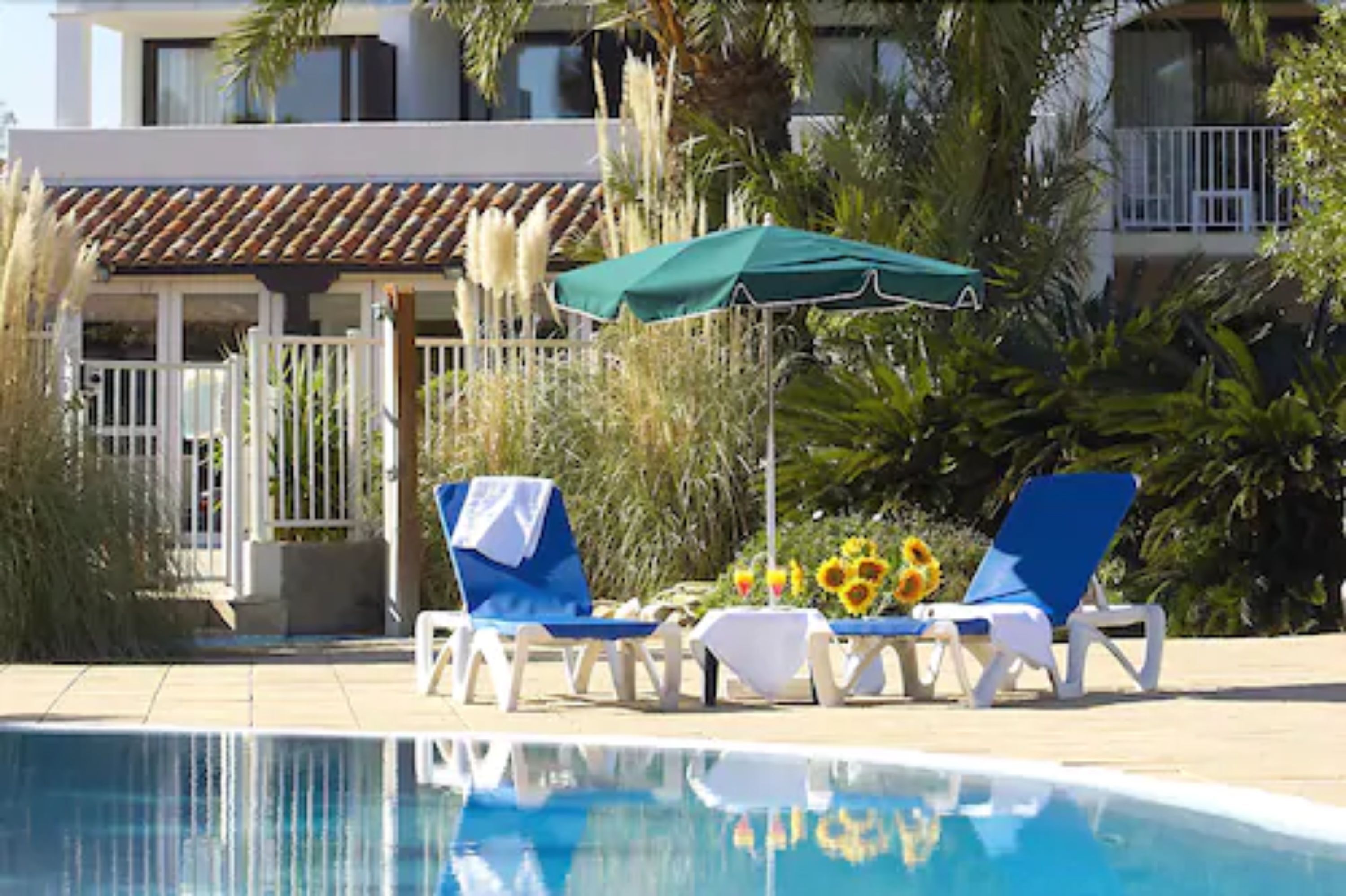 A pool area with lounge chairs, a green umbrella, and sunflowers.