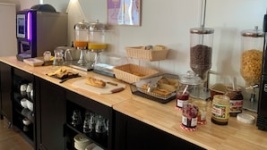 Una barra de desayuno con máquinas de café, dispensadores de jugo, pan, pasteles y salsas.