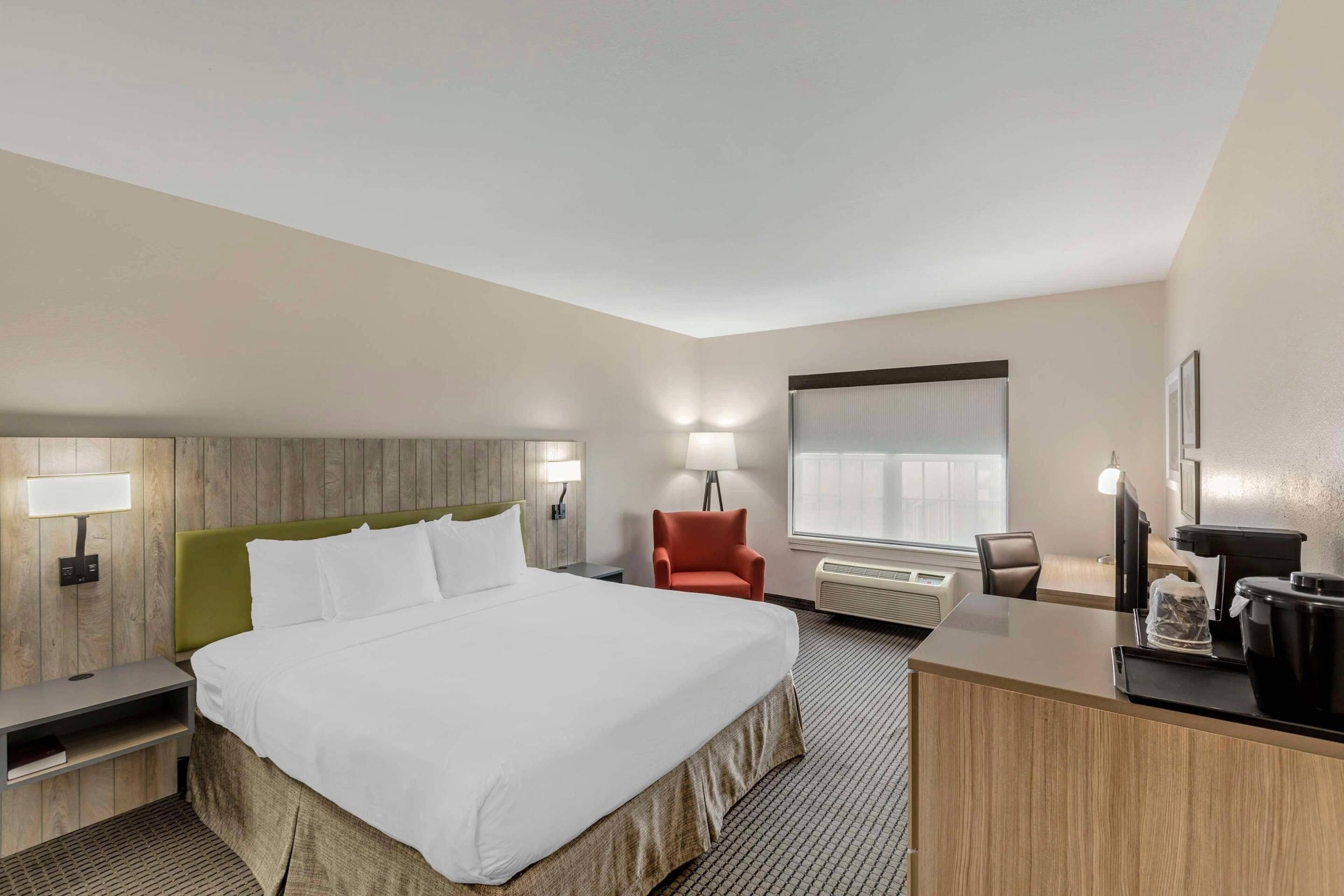 A hotel room with a bed, a desk, a chair, a lamp, and a window.
