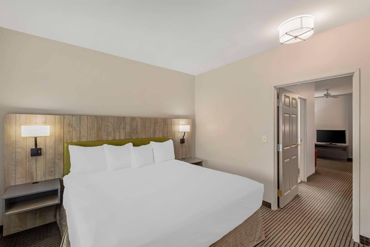 A hotel room with a large bed, two bedside tables, a headboard, a wall-mounted lamp, a ceiling light, and a television in the corner.