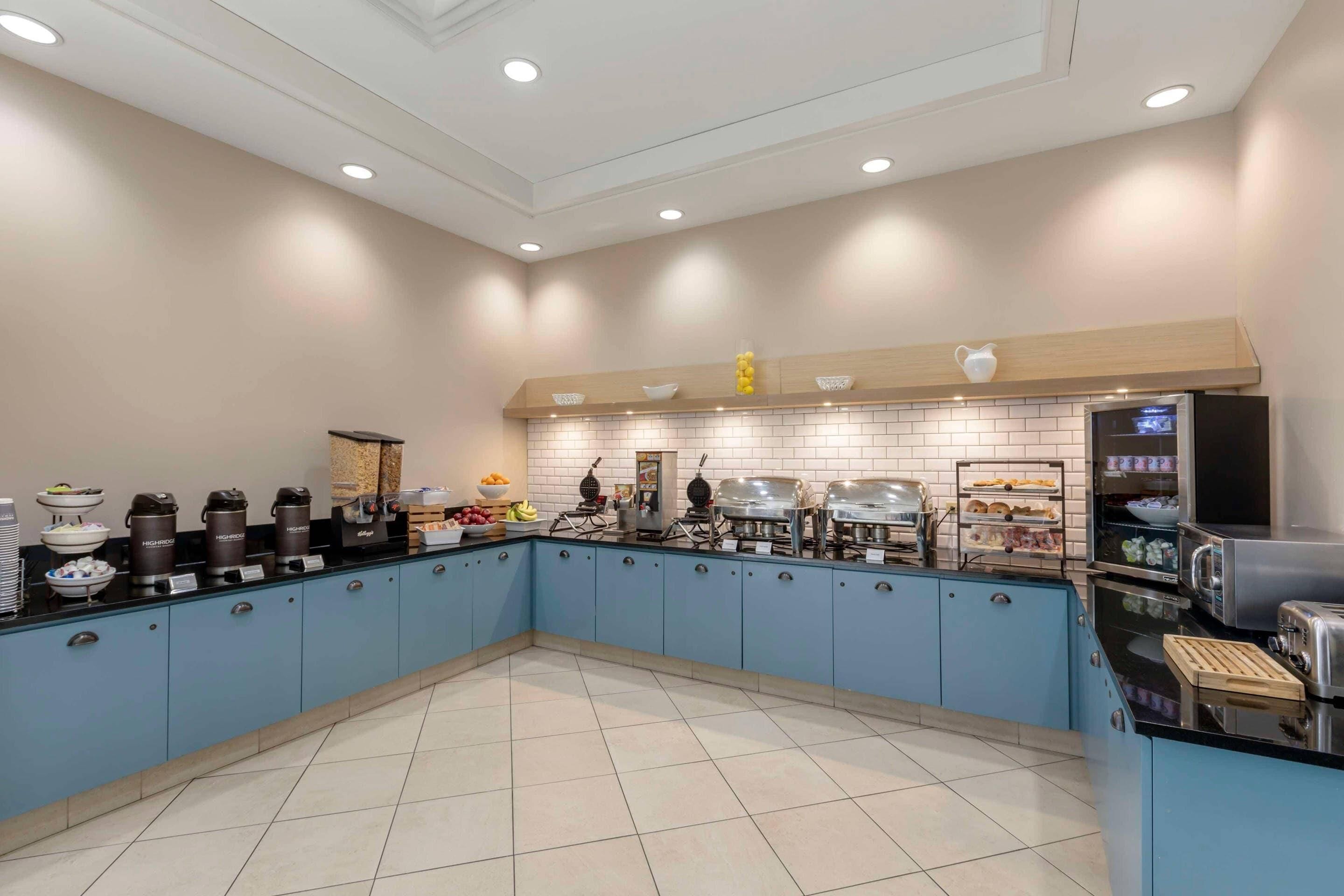 A modern kitchen with blue cabinets, a black countertop, and various appliances.