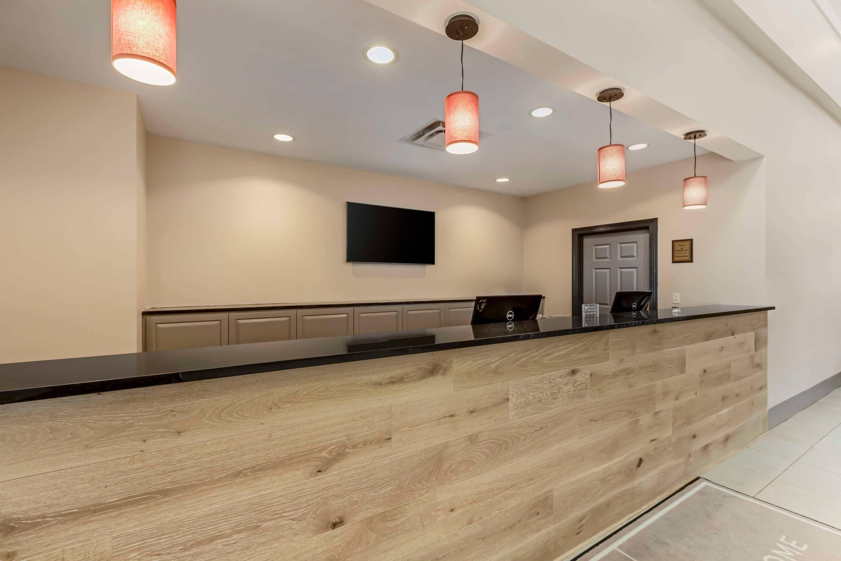 A reception desk with a wooden finish, a flat-screen TV mounted on the wall, and pendant lighting.