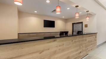 A reception desk with a wooden finish, a flat-screen TV mounted on the wall, and pendant lighting.