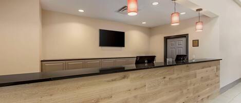 A reception desk with a wooden finish, a flat-screen TV mounted on the wall, and pendant lighting.