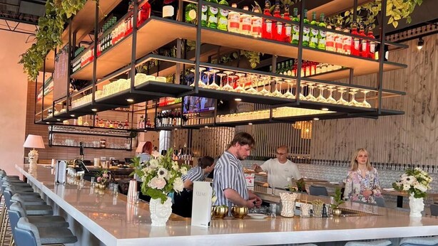 A bar area with multiple shelves of bottles and glasses, bar stools, and a counter with bar staff. - Country Inn & Suites by Radisson, Elk Grove Village/Itasca (Elk Grove Village)