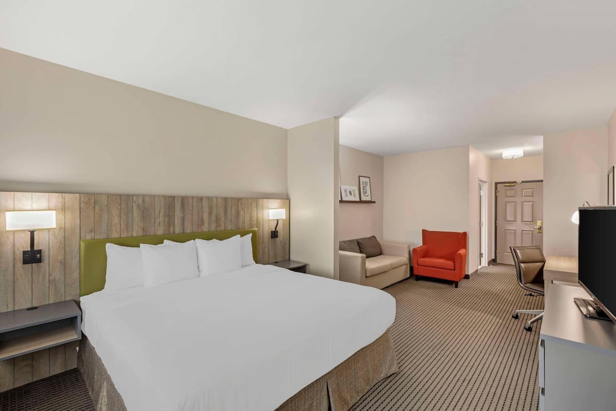 A hotel room with a large bed, a desk with a computer, a chair, and a small table.