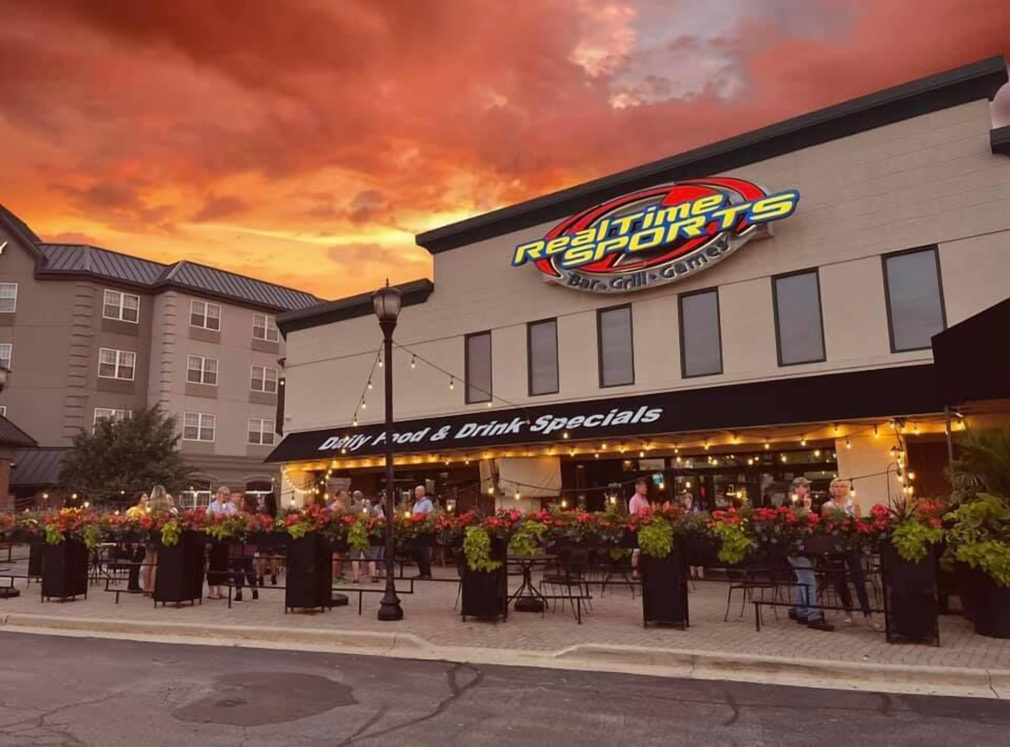 Un restaurant appelé « RealTime Resorts » qui dispose d’une terrasse et affiche une pancarte indiquant les « offres spéciales du jour sur les plats et les boissons ».